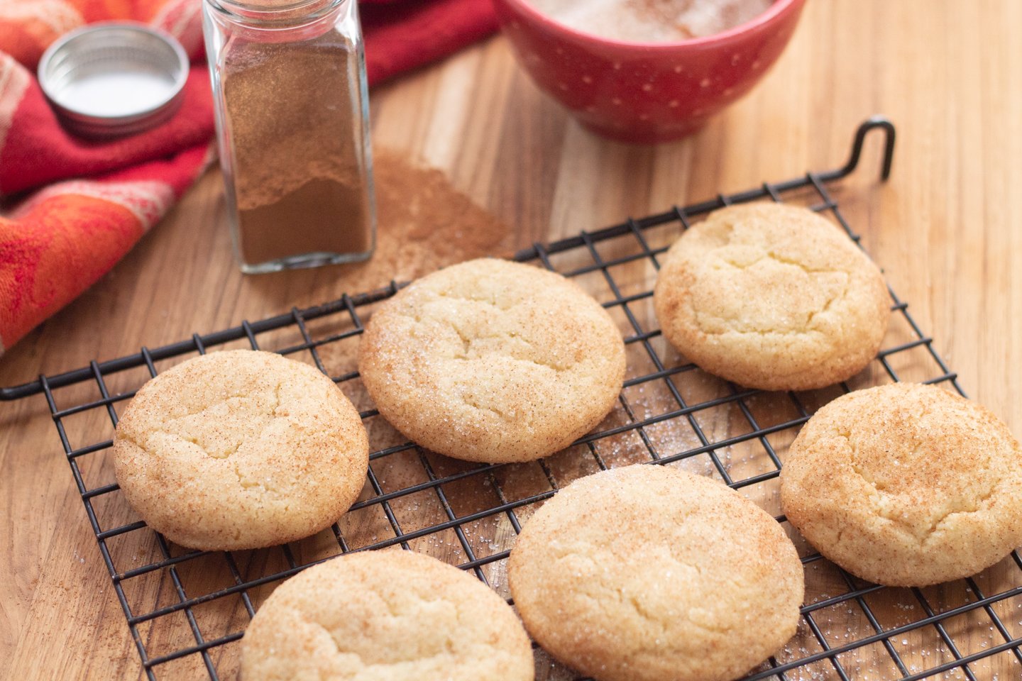 snickerdoodles on baking rack with cinnamon and bowl of sugar