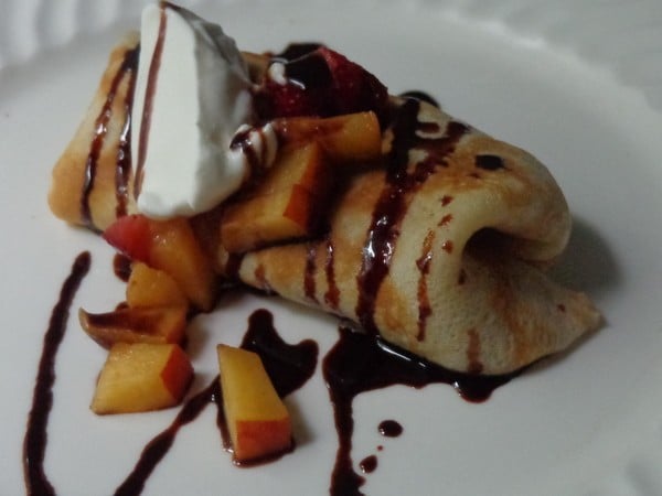 Crepes stuffed with sweetened cream cheese, peaches and strawberries, topped with whipped cream and homemade chocolate sauce