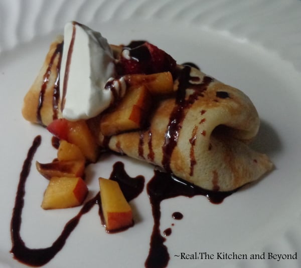 Crepes stuffed with sweetened cream cheese, peaches and strawberries, topped with whipped cream and homemade chocolate sauce
