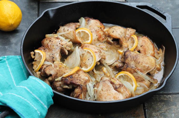 chicken thighs in cast iron pan with lemon and onion blue towel around handle of pan