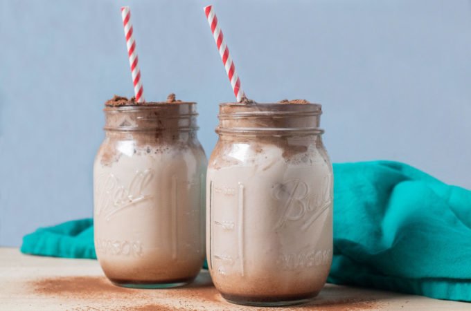 chocolate milk in 2 jars with chocolate whipped topping red striped straw and teal cloth background