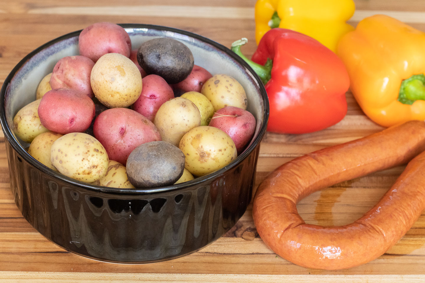 white, red, and purple whole baby potatoes in black bowl; smoked beef ring; red, yellow, and orange bell peppers