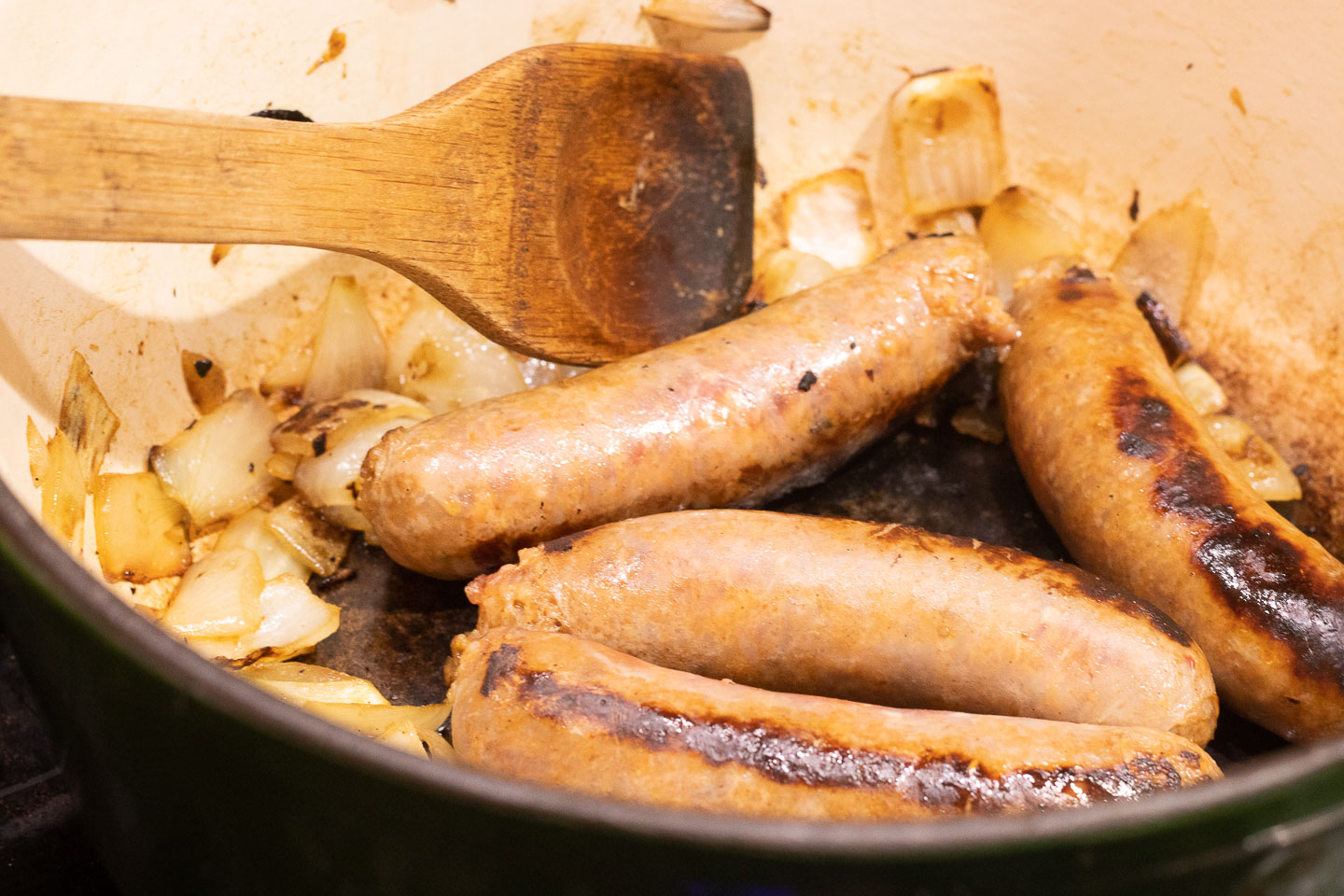 browned sausage links and sauteed onions in enameled dutch oven; brown wooden stirring spoon in pan